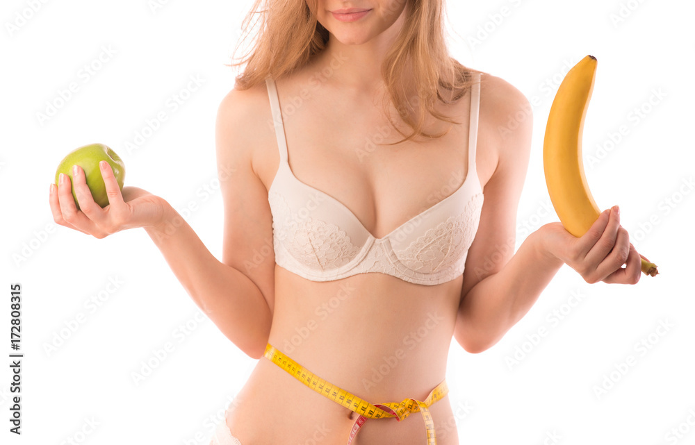 Fitness woman with beautiful body and breasts shows green apple with banana  and measures waist Stock Photo