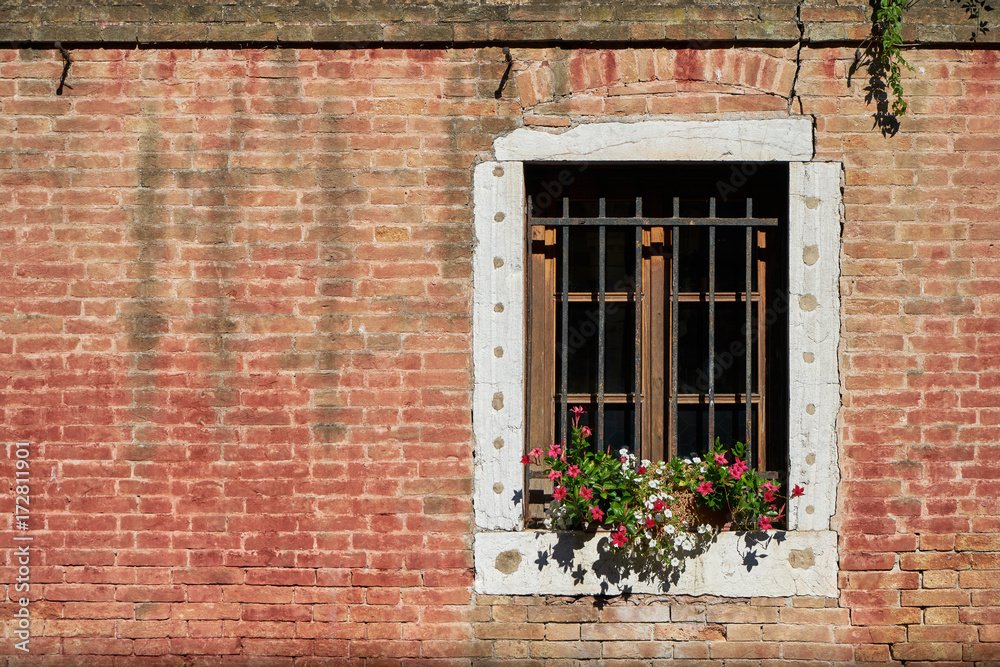 Window with lattice and flowers on the brick wall.Italy