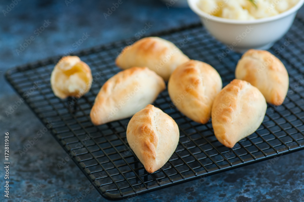 Small mashed potato pasties (hand pies) in a wire rack. Blue stone background. Small mashed potato pasties (hand pies) in a wire rack. Blue stone background.