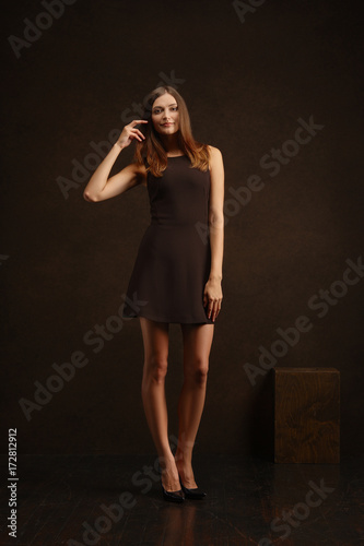 Attractive girl in short dress touching her long hair. Full length low key portrait.