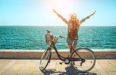 Blonde woman in summer hat with her bicycle walking coastline by
