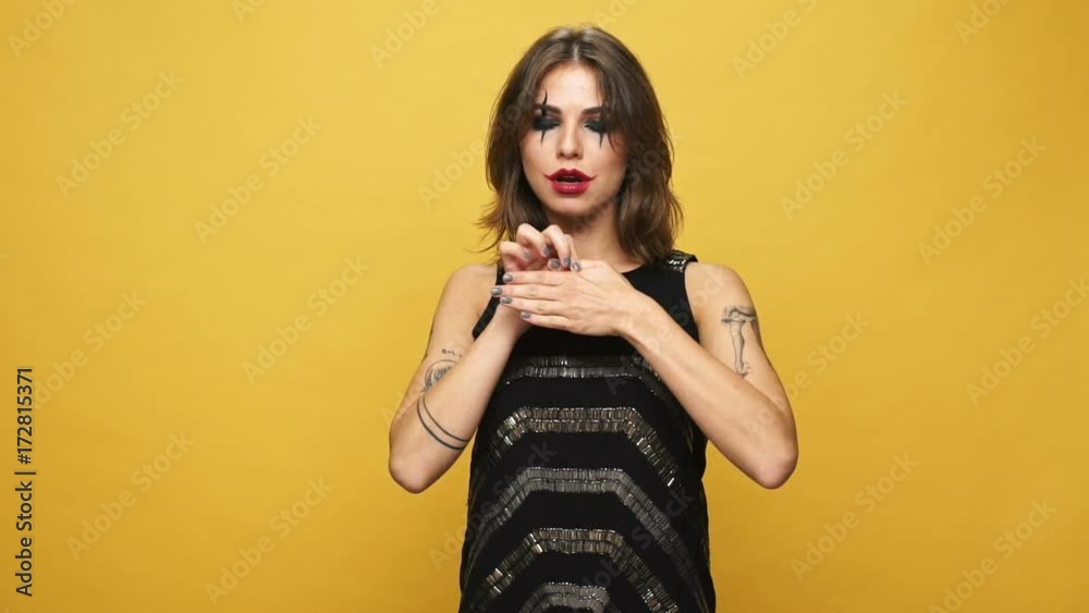 Young strange woman with creepy make up showing focus with finger and laughing isolated over yellow background Young strange woman with creepy make up showing focus with finger and laughing isolated over yellow background