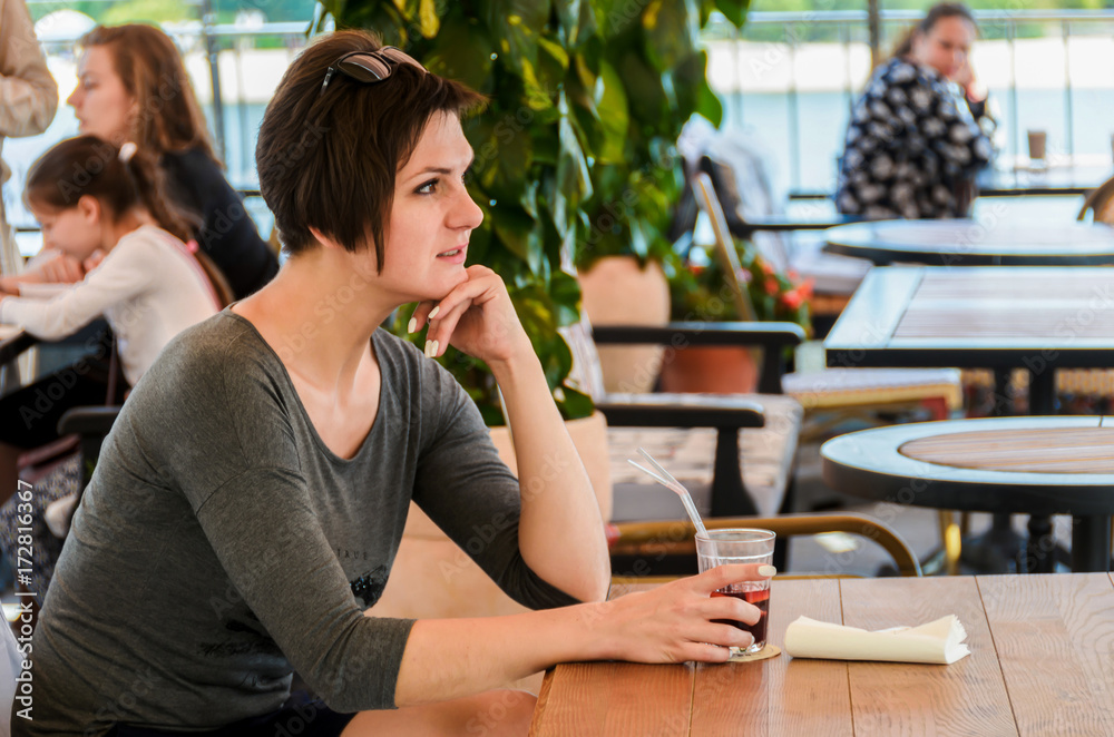 Beautiful woman with short hairdo sits on a summer terrace at a cafe and drinks a cocktail Beautiful woman with short hairdo sits on a summer terrace at a cafe and drinks a cocktail