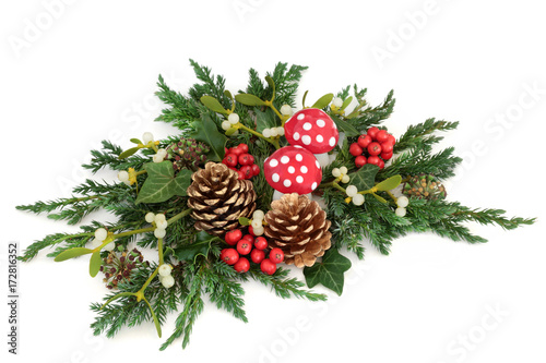 Fantasy christmas decoration with fly agaric mushroom ornaments, holly, ivy, mistletoe and winter greenery with gold pine cones on white background.