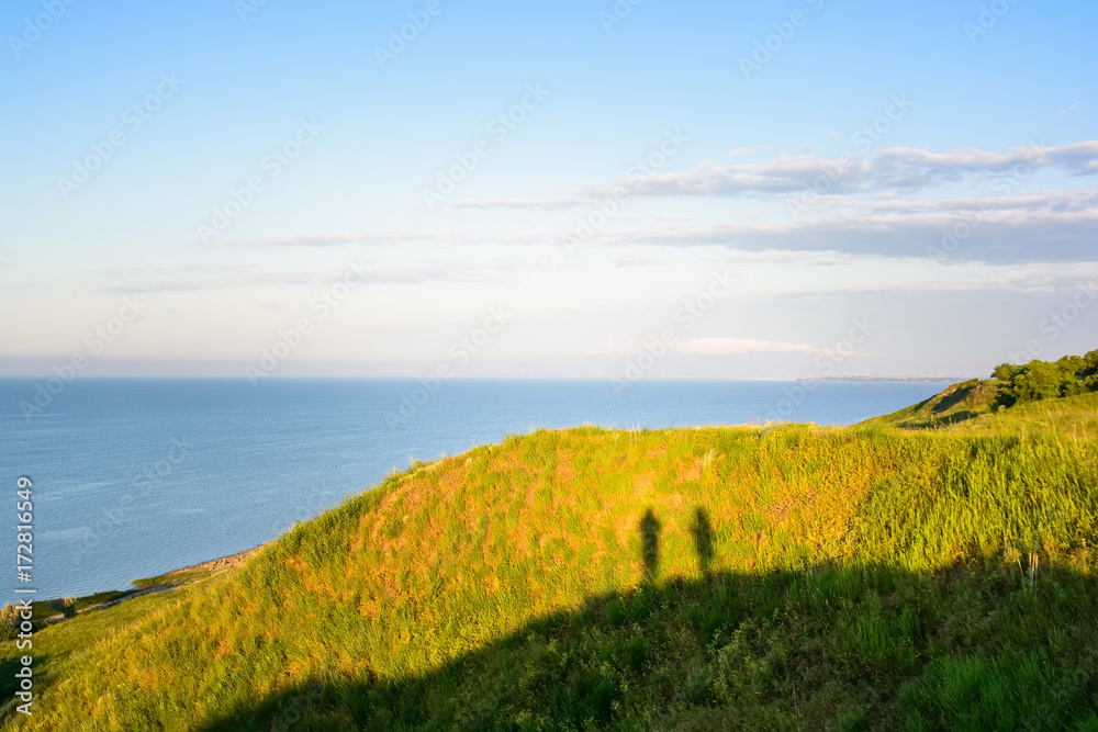 Shadow of two photographers on hill next to sea