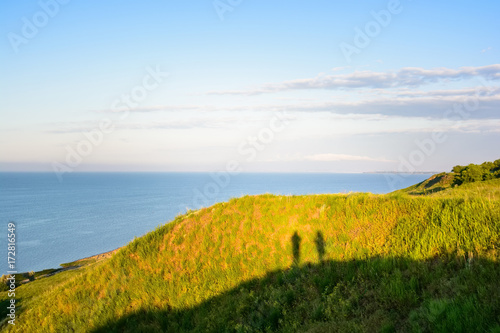 Shadow of two photographers on hill next to sea