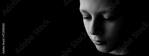 The sad boy with tears in their eyes on a black background