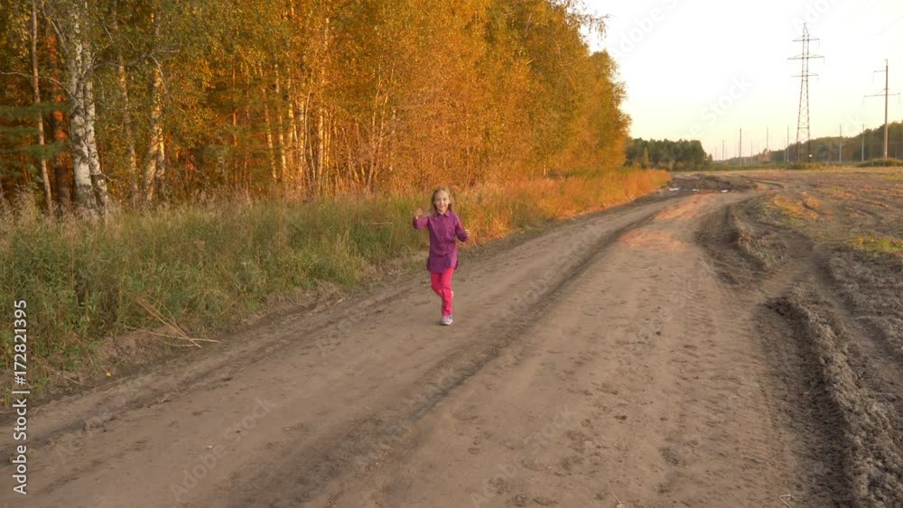Young white girl twisting and turning. Girl jumping by country road at sunset evening. Golden autumn Young white girl twisting and turning. Girl jumping by country road at sunset evening. Golden autumn