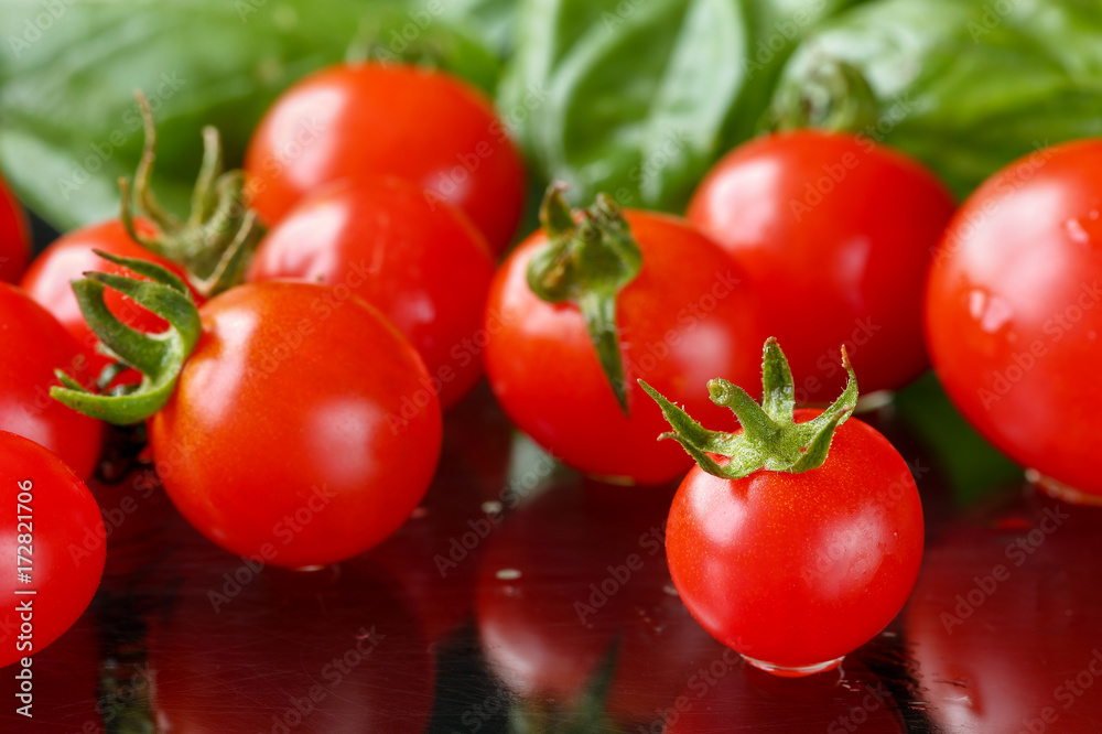 Close up of freshly washed cherry tomatoes on a black cutting board with reflections and basil leaves in background. Selective focus and shallow depth of field Close up of freshly washed cherry tomatoes on a black cutting board with reflections and basil leaves in background. Selective focus and shallow depth of field