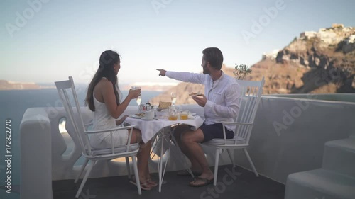 4k travel video couple sitting outside on veranda table enjoying breakfast high up on santorini island with amazing view over the caldera
