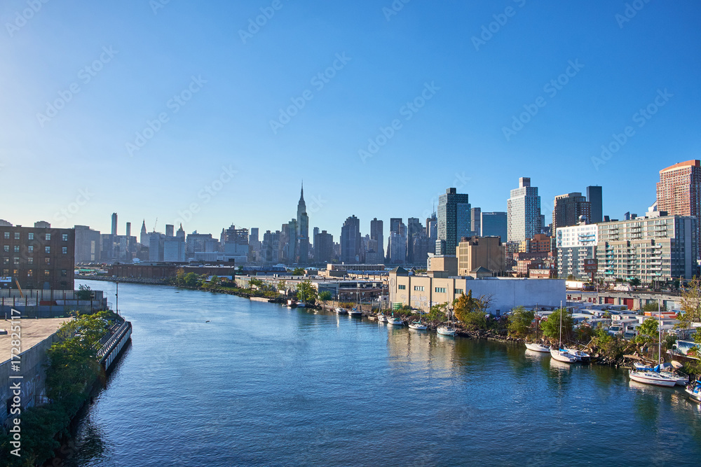 Looking at Manhattan skyline with Empire State Building from Pulaski Bridge in Queens, boats are moored along the river