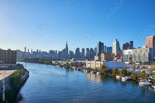 Looking at Manhattan skyline with Empire State Building from Pulaski Bridge in Queens, boats are moored along the river