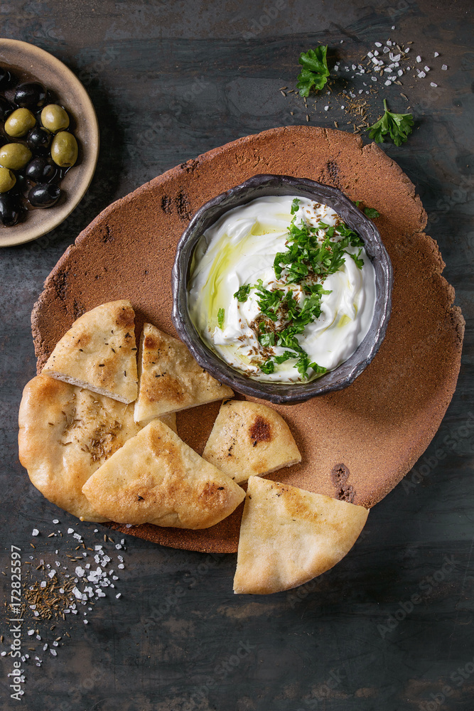 labneh middle eastern lebanese cream cheese dip with olive oil, salt, herbs served with olives, traditional pita bread on terracotta plate over dark texture metal background. Top view with space labneh middle eastern lebanese cream cheese dip with olive oil, salt, herbs served with olives, traditional pita bread on terracotta plate over dark texture metal background. Top view with space