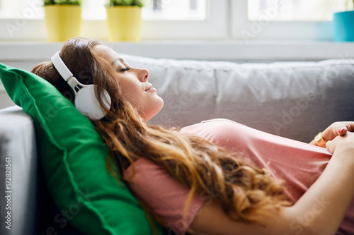 Portrait of a beautiful young woman lying on sofa with headphones on and closed eyes, relaxing photo