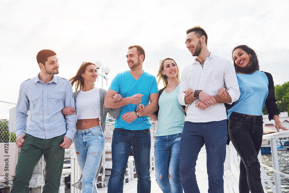 Portrait of a group of young people sitting on the edge of the pier, outdoors in nature. Friends enjoying a game on the lake.