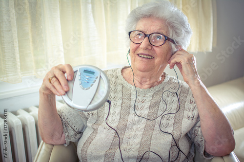 Cheerful senior woman listening to music on CD player at home. photo