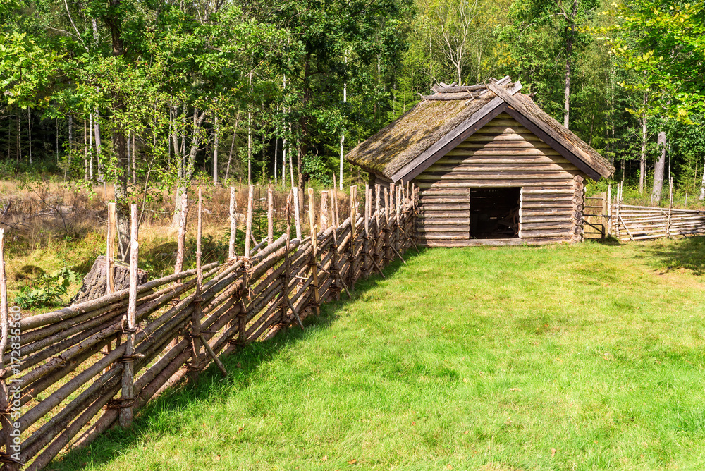 Old wooden storehouse in the woods with wooden fence leading up to it. Old wooden storehouse in the woods with wooden fence leading up to it.