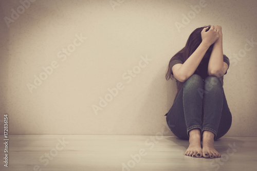 sad woman hug her knee and cry. The depression woman sit on the floor. Teenager girl with depression sitting alone on the floor in the dark room. Toned photo