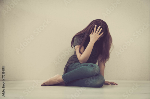 sad woman hug her knee and cry. The depression woman sit on the floor. Teenager girl with depression sitting alone on the floor in the dark room. Toned photo