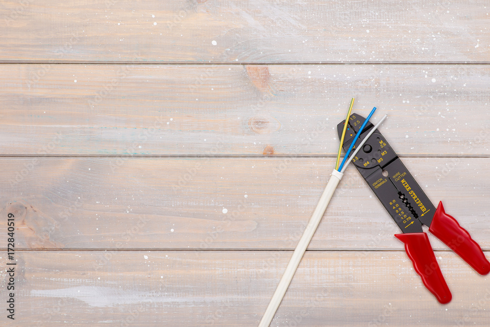 The electrician's tool for stripping and trimming wires lies on a wooden background. There is space for text on the left The electrician's tool for stripping and trimming wires lies on a wooden background. There is space for text on the left