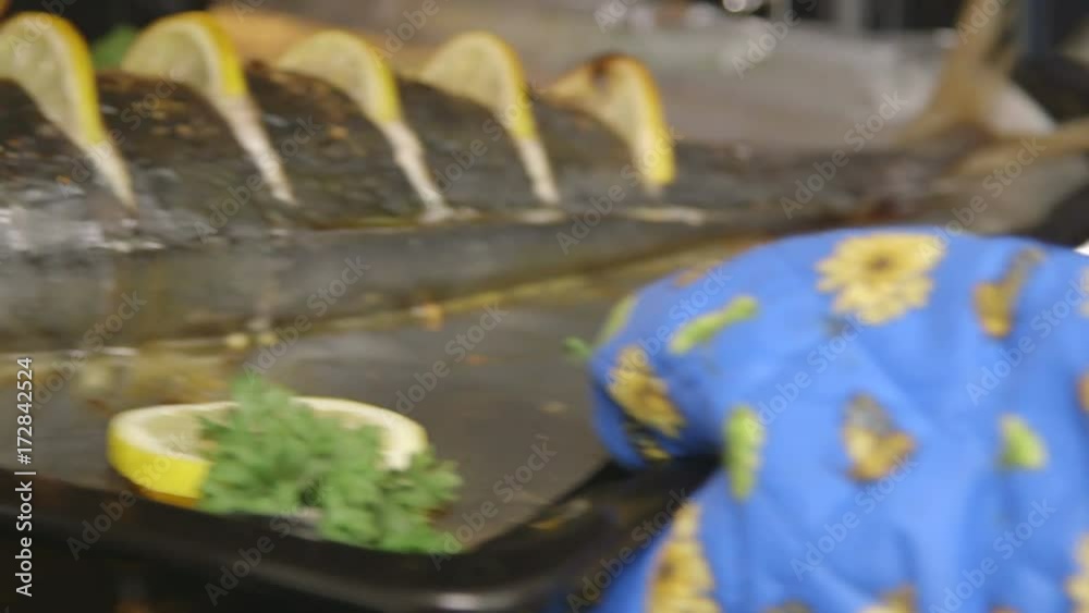 Cooking whole roasted fish seriola with lemon baked in the oven. Chef takes out baking sheet with cooked amberjack from the oven. Food preparation with electric cooker.