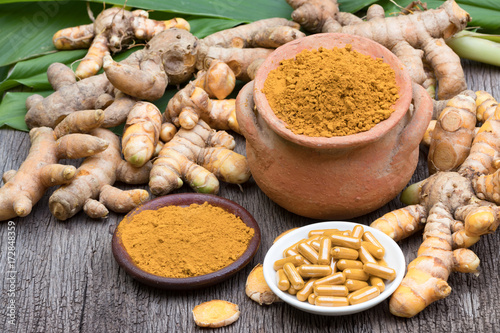 Turmeric powder in clay pot , turmeric capsules and fresh turmeric root on wooden background