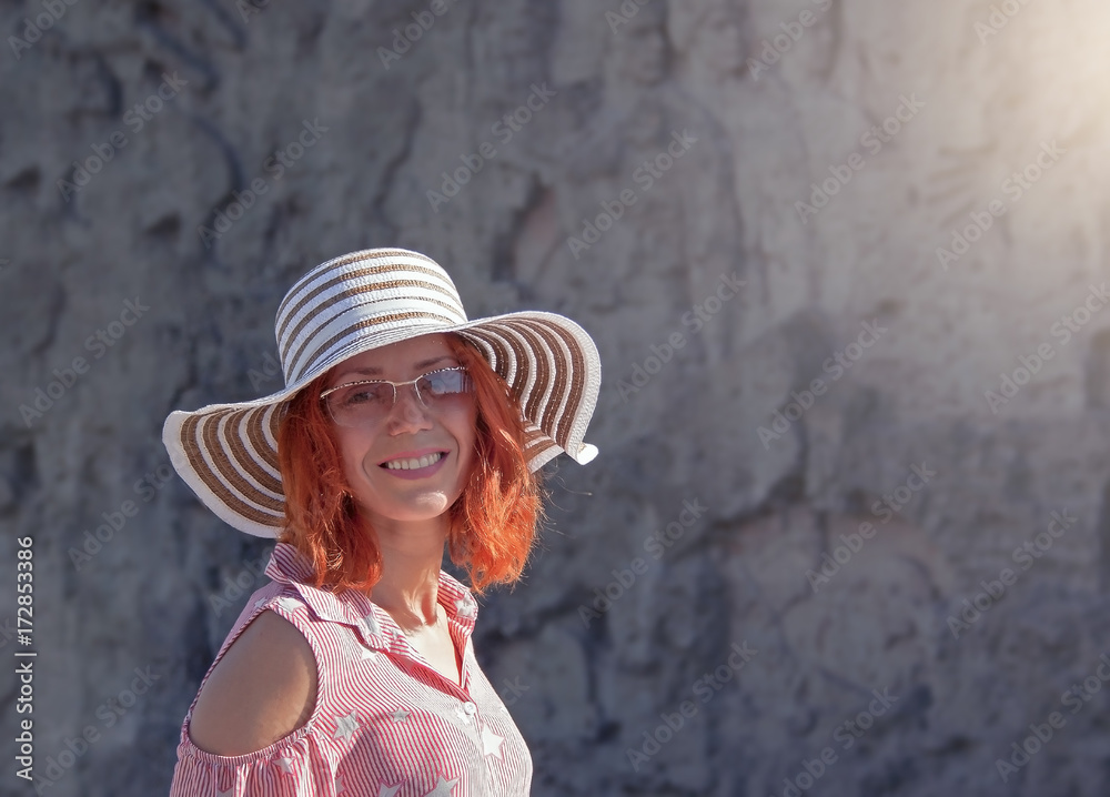 cheerful red-haired young girl in a summer hat and glasses