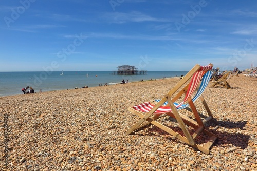 Striped deck chairs on pebble beach in Brighton, England, UK with Brighton West Pier in distance