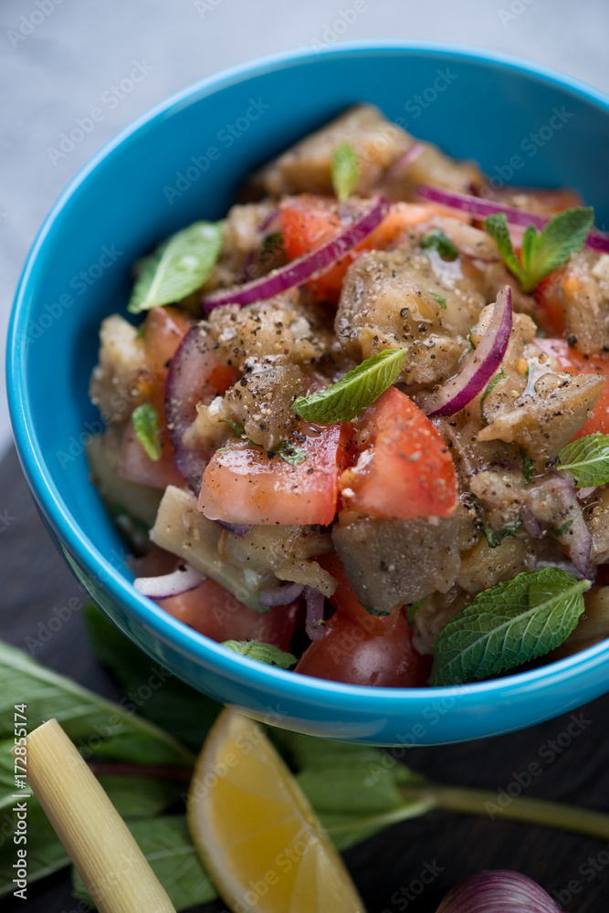 Salad with baked aubergines, fresh tomatoes and mint in a blue bowl, selective focus, close-up, shallow depth of field