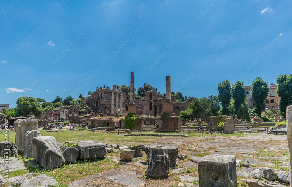 View of the various ruins of the Roman Forum with a very blue sky slightly cloudy without people in sight