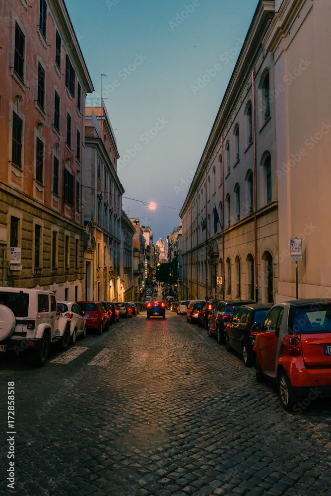 Rome, Lazio, Italy. May 26, 2017 : Typical narrow cobbled shopping street of Rome, Italy. With people walking at dusk