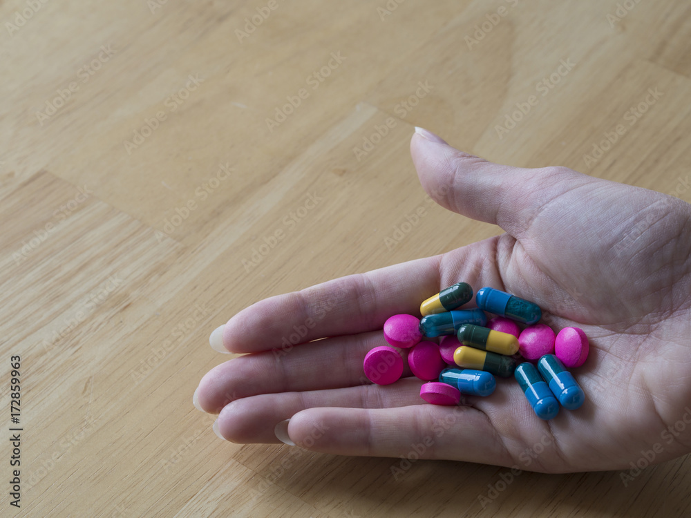 women hand full of colorful blue green yellow and pink pills pain killers and antibiotic capsule wooden background