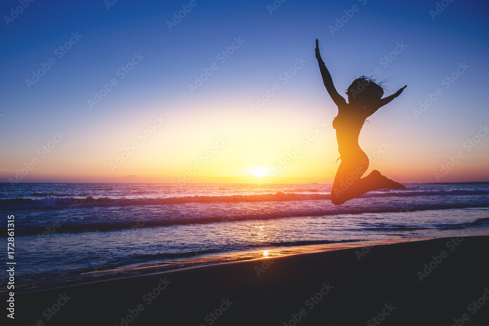 Silhouettes. Girl is jumping beach with beautiful sunset in background