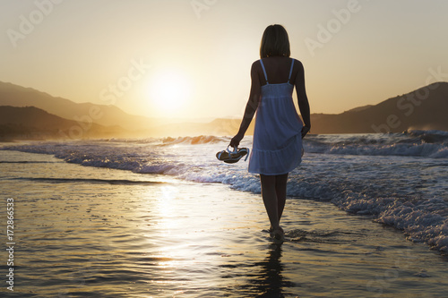 Fototapeta Naklejka Na Ścianę i Meble -  A girl is walking along Crete island coastline at the sunset time.