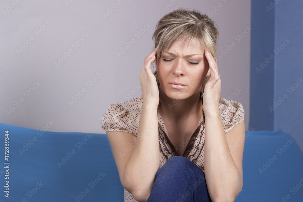 Obraz premium Young woman sitting on a couch, holding her head, having a strong headache