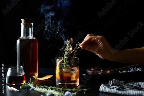 Woman's hand holding burning match in glass of maple cocktail