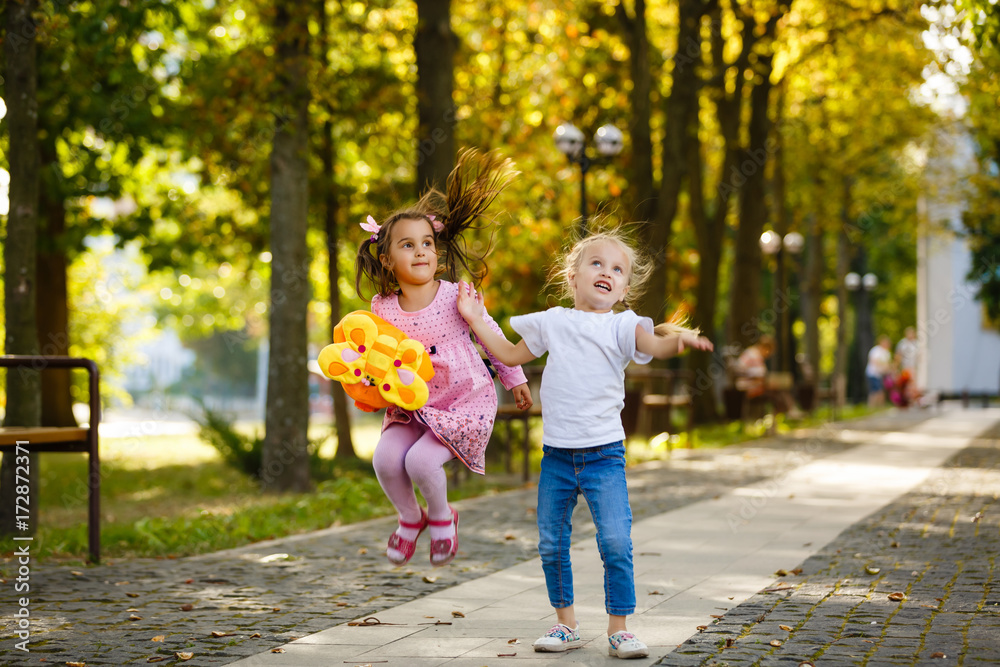 Fototapeta premium two happy little schoolgirls jumping and throwing a backpack
