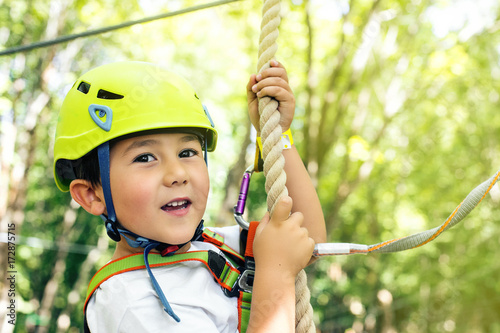 Happy little boy passing the cable route high among trees, climbing and playing, extreme sport in adventure park
