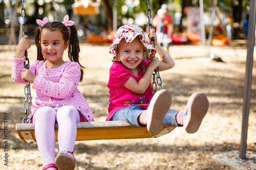 Two beautiful little girls on a swings outdoor in the playground at summertime