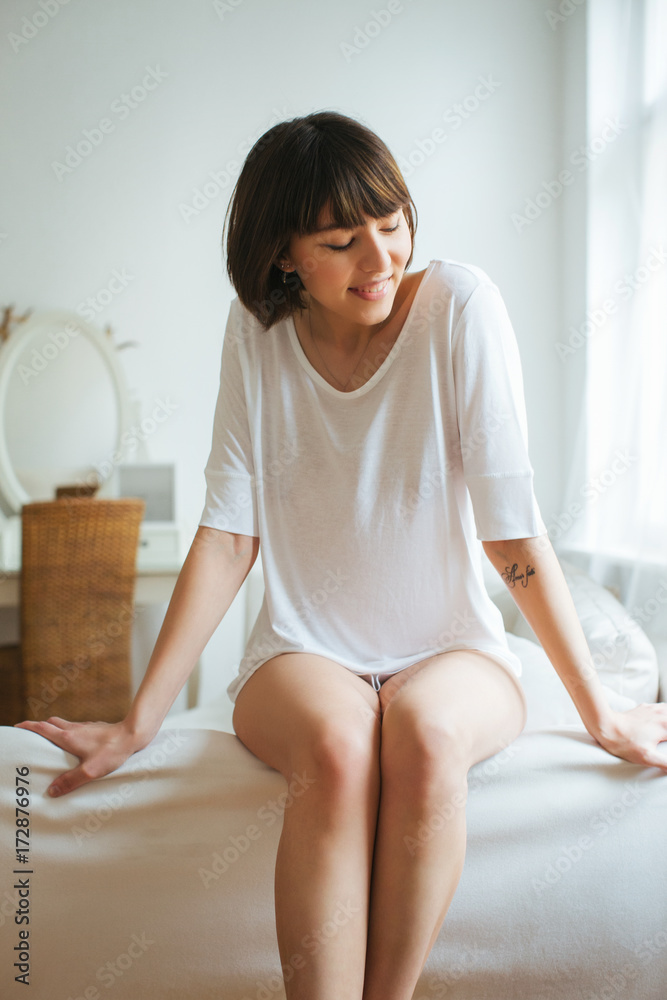 Indoor Portrait of Young Smiling Caucasian Woman Sitting in White Bedroom Indoor Portrait of Young Smiling Caucasian Woman Sitting in White Bedroom