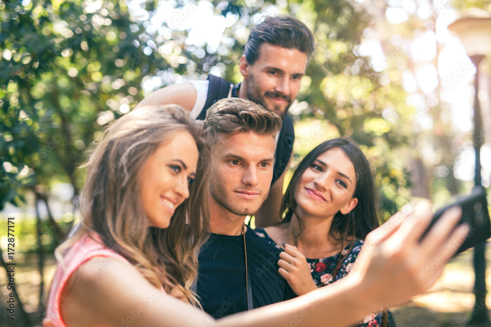 Group of four funny friends taking selfie with a smart phone in summer park