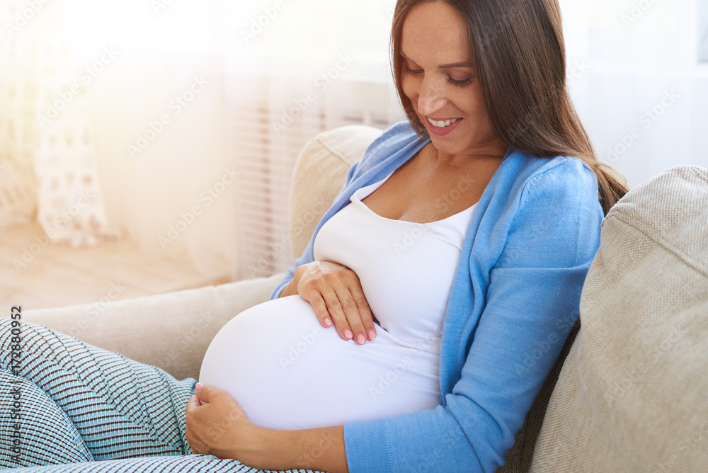 Pregnant woman holding her belly with arms on sofa