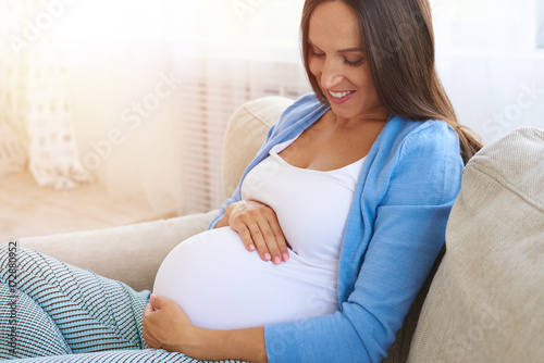 Pregnant woman holding her belly with arms on sofa