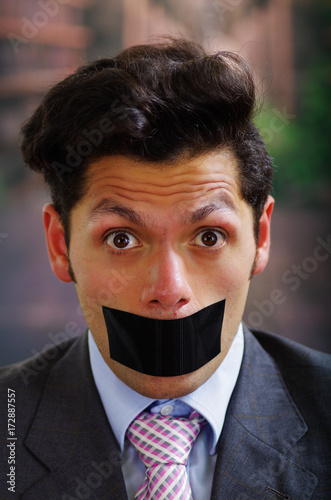 Portrait of a desperate businessman, with a black tape in his mouth, in a blurred background photo