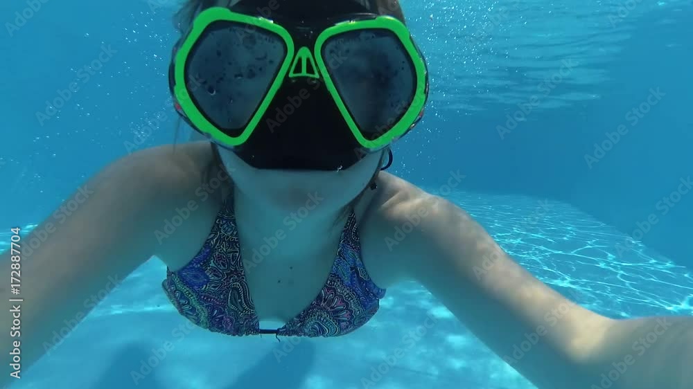 happy girl with a mask in a swimming pool underwater swims takes the ...