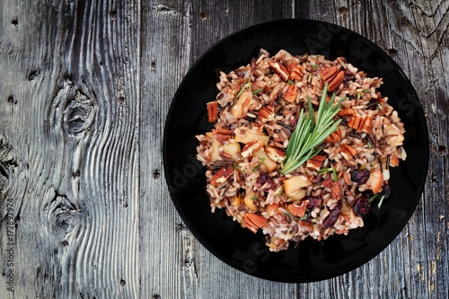 Autumn rice pilaf with apples and cranberries in a black plate against an old wood background