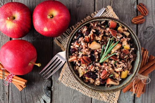 Autumn rice pilaf with apples, nuts and cranberries, overhead scene against a rustic wood background