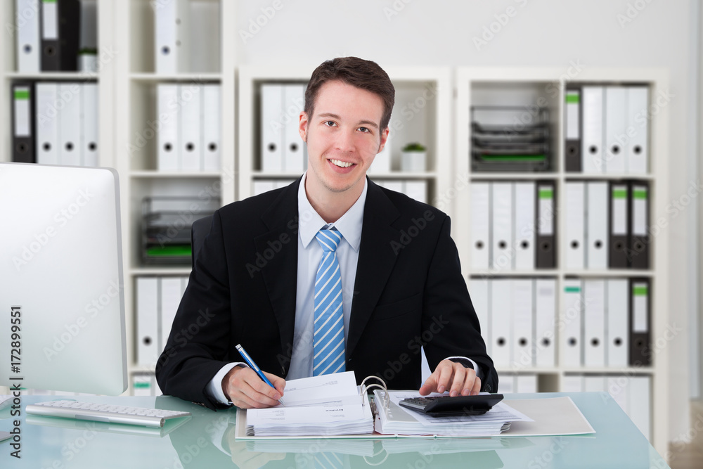 Fototapeta premium Confident Businessman Using Calculator At Office Desk
