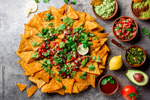 Nachos. Totopos with sauces. Mexican food concept. Yellow corn totopos chips with different sauces salsas - pico del gallo, guacamole, salsa verde, chili pebre and fresh avocado, tomatoes, lemon and photo