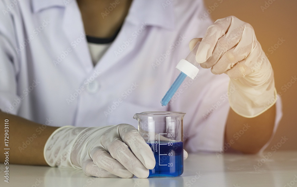 The doctor holds a dropper with a blue vaccine inside beaker. Vaccines help build immunity and disease prevention. Laboratory room. Close up and blur. The doctor holds a dropper with a blue vaccine inside beaker. Vaccines help build immunity and disease prevention. Laboratory room. Close up and blur.